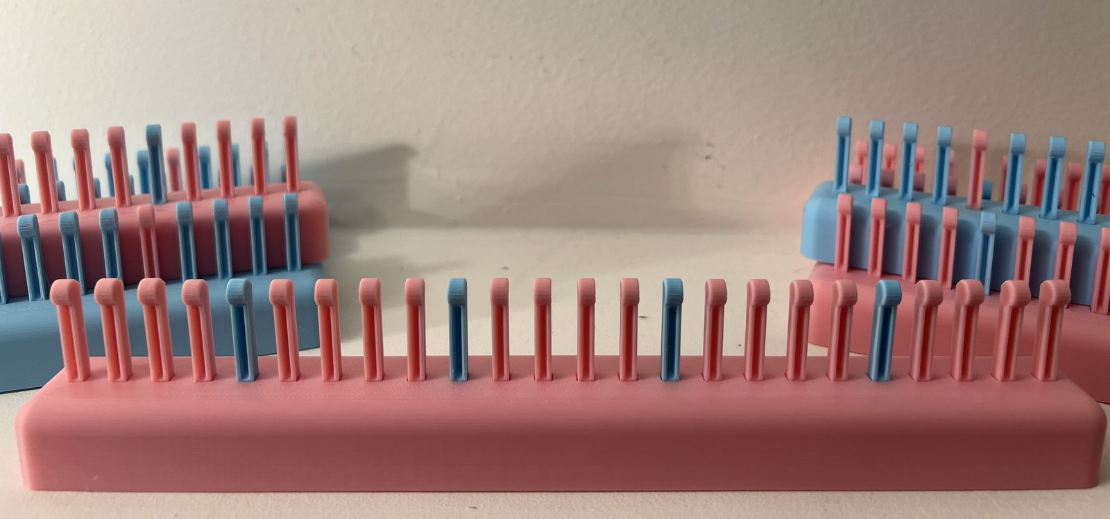 Several knitting looms in pink and blue, their pegs alternating between the two colors
